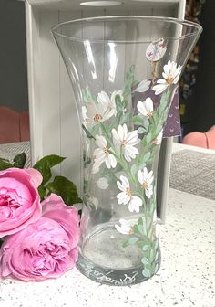 two pink roses sitting next to a vase with flowers painted on the inside and outside