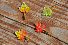 four beaded autumn leaves are sitting on a wooden surface, one is yellow and the other is orange