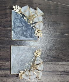 two square pieces of glass with gold leaves on them sitting on a wooden table next to each other