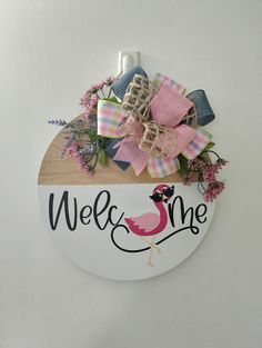 a welcome sign hanging from the side of a white wall with pink and blue flowers