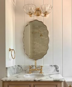 a bathroom vanity with marble counter top and gold faucet, two lights on the wall