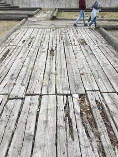 two people walking across an old wooden bridge