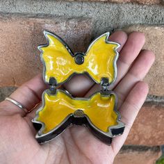 a yellow and black dog bone brooch in someone's hand on a brick wall