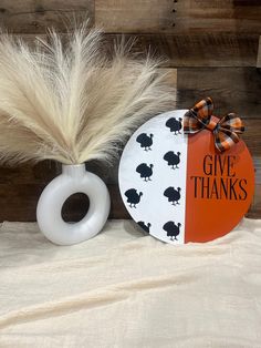 an orange and white sign sitting on top of a table next to a vase filled with feathers