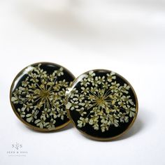 two black and gold dandelion earrings sitting on top of a white table next to each other