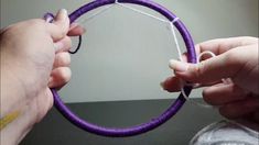 two hands are holding a purple object with white yarn on it and one hand is tying the string