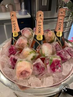 four bottles of champagne on ice in a bowl with pink flowers and roses around it