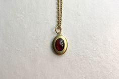 "This sweet, small, OVAL antique brass locket has a smooth Natural Garnet cabochon set on the front.  It hangs on a 16\" gold stainless steel chain necklace.  The locket is approximately 11x16mm.  The cabochon is 6x8mm.  Arrives in an eco-friendly jewelry box, ready for gifting. MORE lockets in my shop! FREE SHIPPING! THANK YOU FOR VISITING MY SHOP!" Classic Brass Jewelry With Cabochon, Antique Gold Oval Cabochon Necklace, Antique Gold Necklace With Oval Cabochon, Classic Vintage Charm Brass Necklace, Victorian Gold Necklace With Oval Cabochon, Victorian Gold Oval Cabochon Necklace, Antique Finish Yellow Gold Necklace For Gift, Oval Cabochon Brass Necklace, Classic Brass Locket Necklace With Vintage Charm