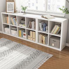 a white bookcase with many books on it in a living room next to a window