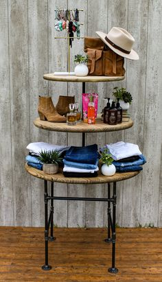 three tiered shelf with hats, clothing and other items on it in front of a wooden wall