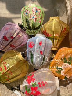 many different colored lanterns with flowers on them are sitting on a tablecloth covered surface