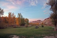 an empty picnic table in the middle of a grassy field with mountains in the background