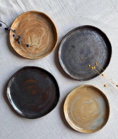 three black and brown plates sitting on top of a white cloth covered table next to dried flowers