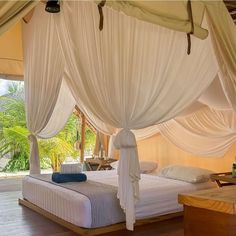 a canopy bed with white drapes on top of it in a room filled with wooden floors