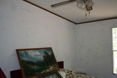 a bed with a painting on top of it next to a ceiling fan and window