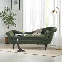 a green couch sitting on top of a white rug next to a table with a plant