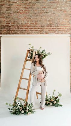 a pregnant woman standing in front of a ladder with flowers and greenery on it