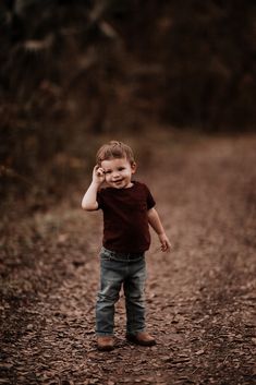 a little boy standing in the middle of a dirt road talking on a cell phone