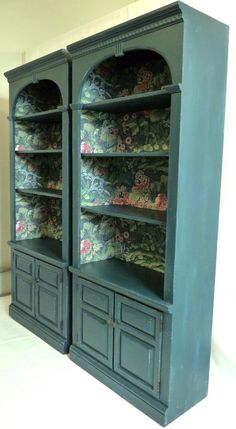 a green bookcase with floral wallpaper on it