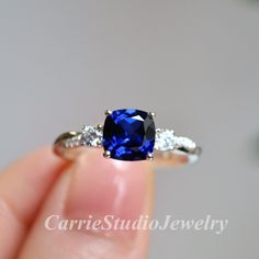 a woman's hand holding an engagement ring with a blue sapphire and diamond accents