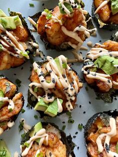 an assortment of sushi rolls with sauce drizzled over them and garnished with avocado