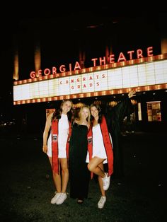 three girls standing in front of a marquee at night