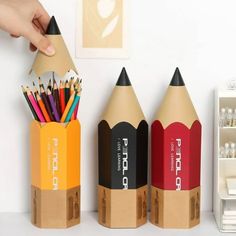 three colored pencils are placed next to each other on a desk with a person's hand reaching for them