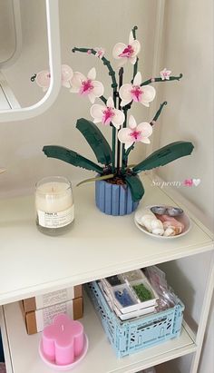 a white shelf topped with a vase filled with flowers next to a candle and other items