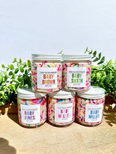 four jars of baby candles sitting on top of a wooden table next to green plants