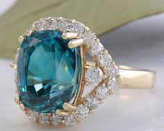 8.70 Carats Natural Very Nice Looking Blue Zircon and Diamond 14K Yellow Gold Ring Suggested Replacement Value: 9,000.00 Total Natural Cushion Shaped Zircon Weights: Approx. 7.80 Carats Zircon Measures: 11 x 8.4mm Natural Round Diamonds Weight: .90 Carats (color G-H / Clarity SI1-SI2) Ring total weight: 5.2 grams Disclaimer: all weights, measurements and colors are approximate and may vary slightly from the listed dimensions or as seen in the image. All pictures are magnified to show the smalles Blue Emerald Halo Setting Ring, Blue Emerald Rings With Halo Setting, Blue Emerald Ring With Round Cut, Blue Emerald Ring With Halo Setting, Turquoise Sapphire Ring For Anniversary, Blue Diamond Emerald Ring In Fine Jewelry Style, Blue Gia Certified Emerald Ring For Formal Occasions, Blue Oval Emerald Ring With Brilliant Cut, Luxury Blue Topaz Ring Gia Certified