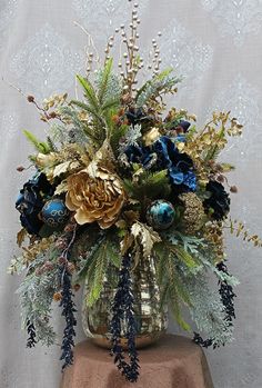 a vase filled with blue and gold flowers on top of a brown tablecloth covered surface