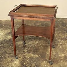 a small wooden table with wheels on the bottom and an open shelf below it that has a leather top