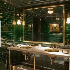 a green tiled bathroom with two sinks and mirrors on the wall in front of it