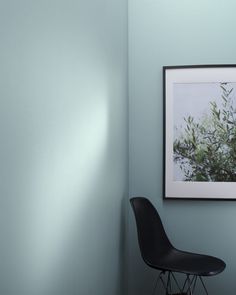 a black chair sitting in front of a blue wall with a picture hanging on it