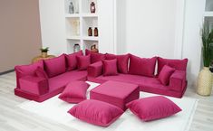 a living room filled with pink couches and pillows on top of a white rug