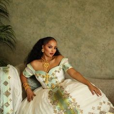 a woman sitting on top of a couch wearing a white dress and gold necklaces