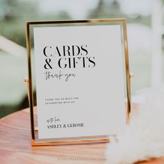 a card and gifts sign sitting on top of a wooden table next to a feather