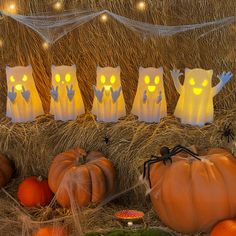 some pumpkins are sitting in hay with lights on them and ghost bags behind them