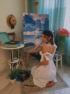 a woman is sitting on the floor in front of an easel with a painting