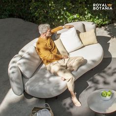 an older man sitting on a white couch in the shade with his feet propped up