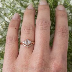 a woman's hand with a ring on it and some flowers in the background