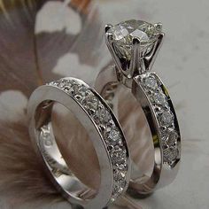 two white gold wedding rings with diamonds on each one and a feather in the background