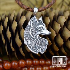 a silver wolf head on a brown leather cord necklace with beads and pine cones in the background