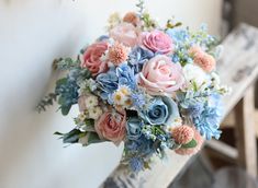 a bridal bouquet with pink, blue and white flowers on a wooden bench in front of a wall