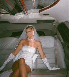 a woman sitting in the back seat of a car wearing white gloves and a wedding dress