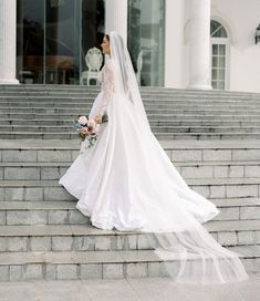 a woman in a wedding dress is standing on some steps with her veil over her head