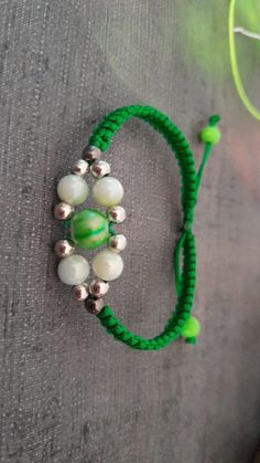 a green and white beaded bracelet sitting on top of a gray cloth covered floor