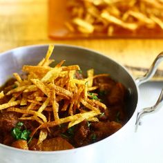 a silver bowl filled with meat and french fries on top of a wooden cutting board