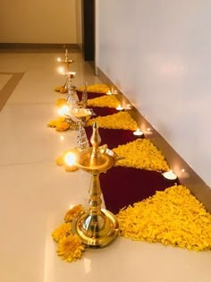 a row of gold candles sitting on top of a white floor next to yellow flowers