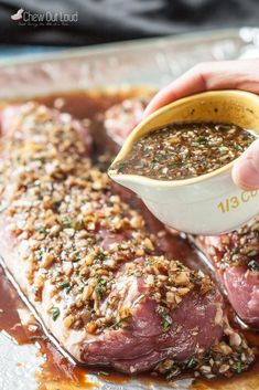 a person pouring sauce on top of some meat